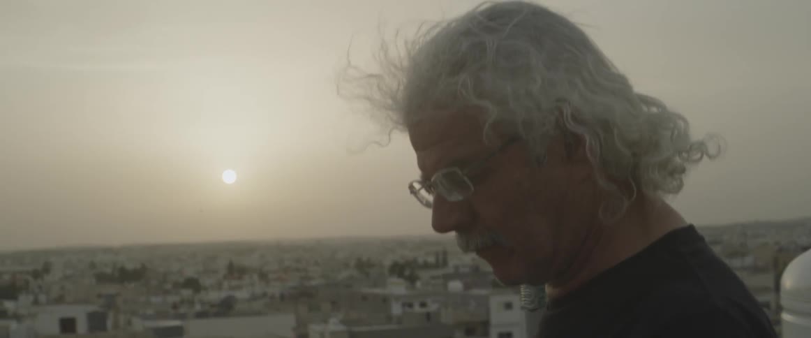 The wind blows a man's hair as he stands outside at dusk