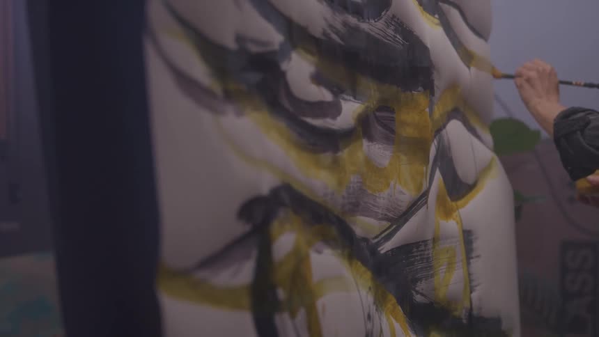 A painter is painting bold strokes of yellow and black paint on a light weight canvas
