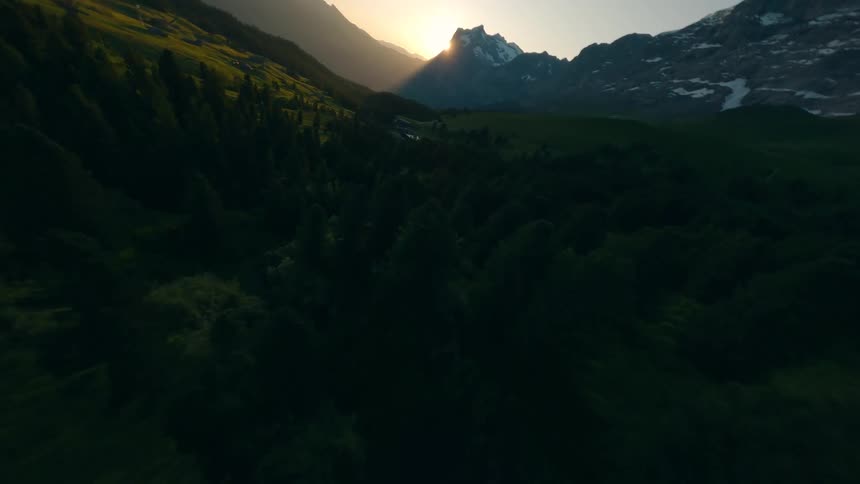 Sunlight breaks over mountains lighting a forested valley at dawn