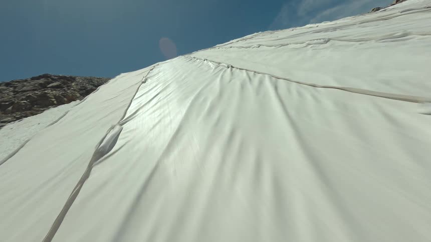 A drone captures a snowy mountain slope under a clear blue sky