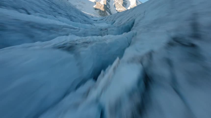Blue ice formations stretch across a glacier at the base of snowcovered swiss mountains