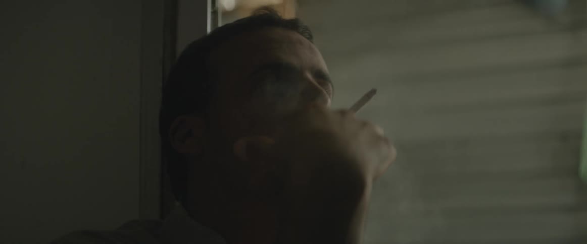 A man smokes a cigarette next to a window