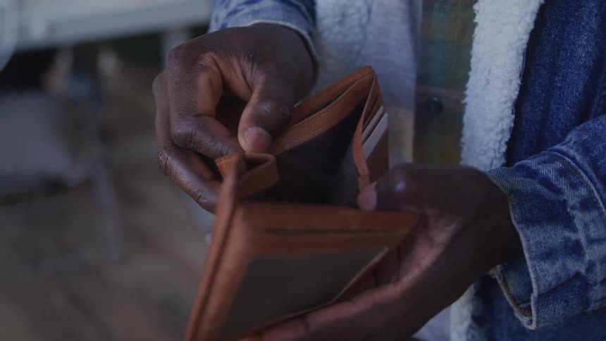 Man looks through an empty wallet while standing on a wooden floor