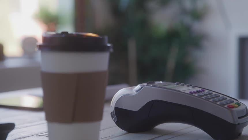A person swiping a card on a credit card machine while taking a cup of coffee from someone else