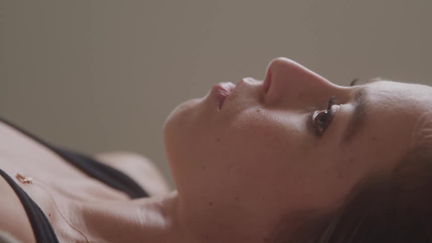 Woman lying down gazes upward with a contemplative expression under soft neutral light