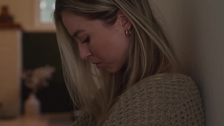 Woman leans against the wall with an introspective expression and downward gaze