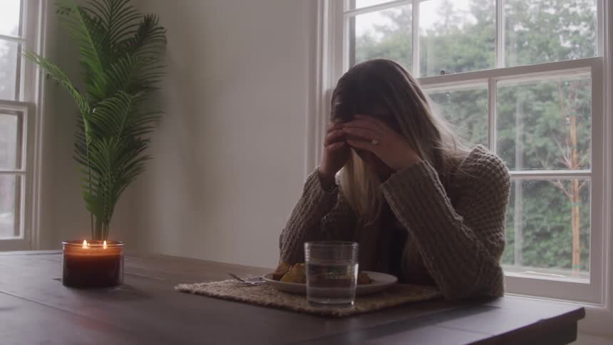 A woman sadly sits at the dinner table