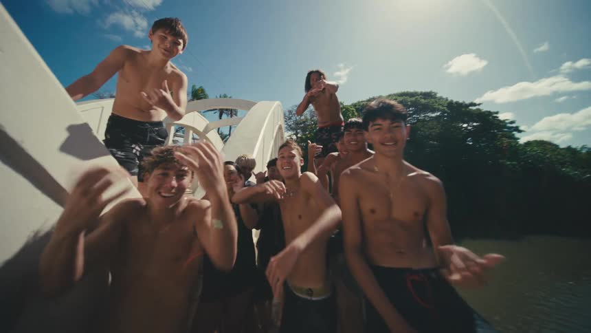 Group of shirtless teenagers with happy expressions on a bridge over a river