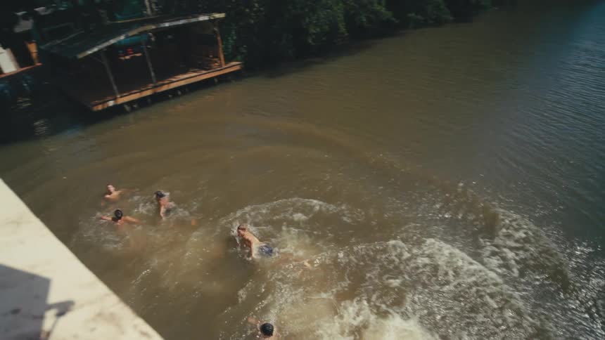 Group of people swims toward a wooden deck in a darkwater river