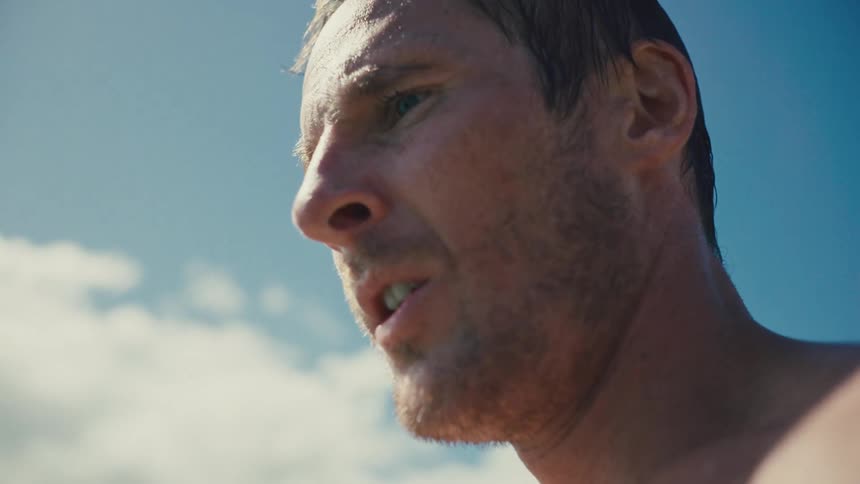 A shirtless man stands outdoors at midday taking a deep breath before jumping