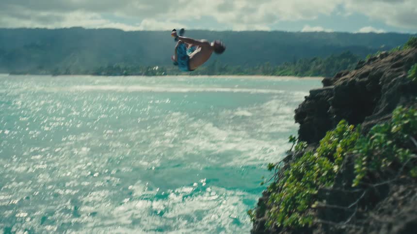 Man holding a camera while standing on a cliff and jumping towards the sea