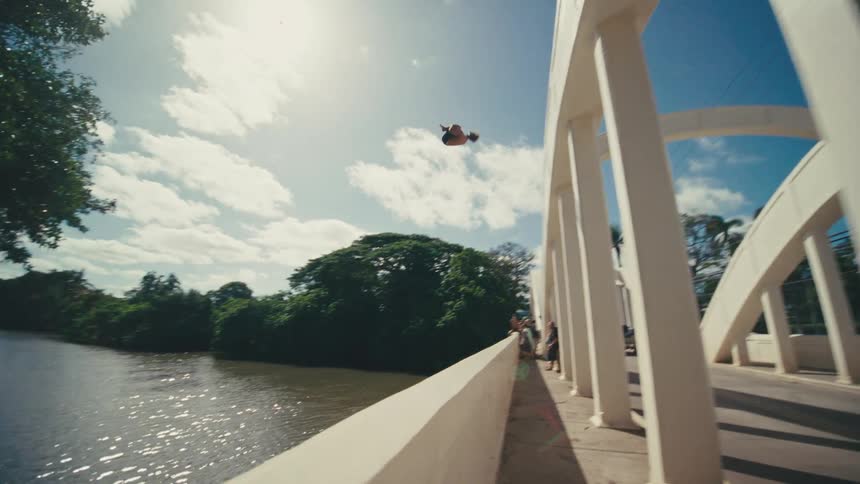 The man does a flip off the bridge into the river