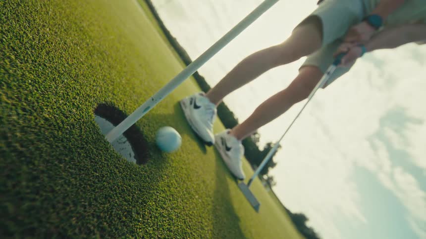 Man hitting a golf ball and then taking the white ball from the hole