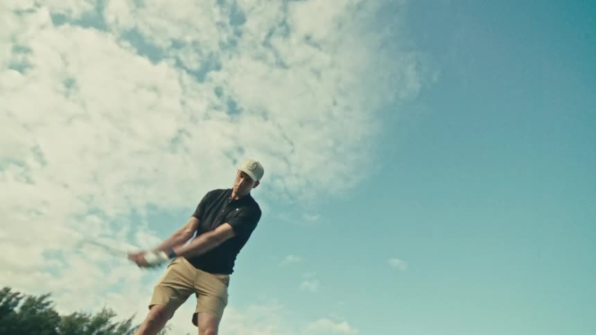 A golfer swings at a golf ball on a golf course at midday