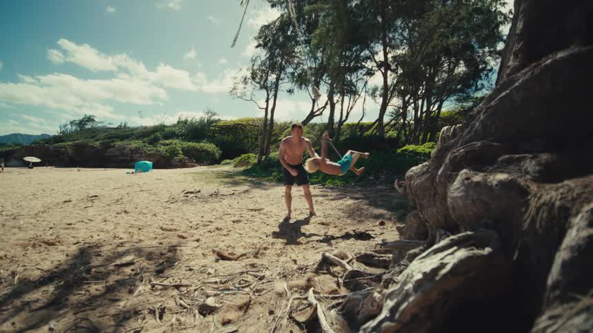 A father pushes his son on a tree swing on the beach