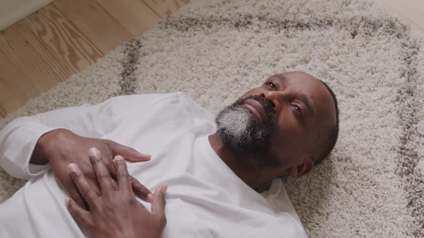 Man lying on the light carpet rests with hands on his chest and gaze turned upward