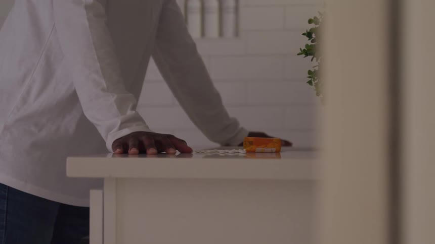 Man rests his hands on the kitchen counter in front of a pill bottle