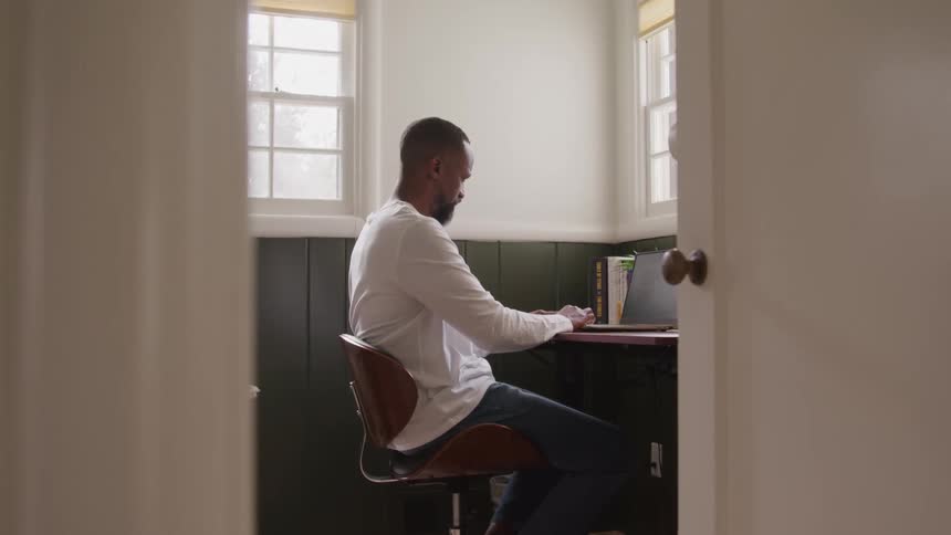 Man sitting on a chair types on a laptop placed on a wallmounted desk
