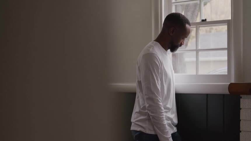 Man with his head down next to a window in a room of the house