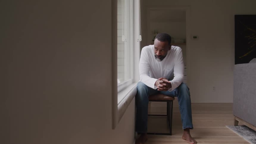 Man sitting by the window looking outside with a thoughtful expression
