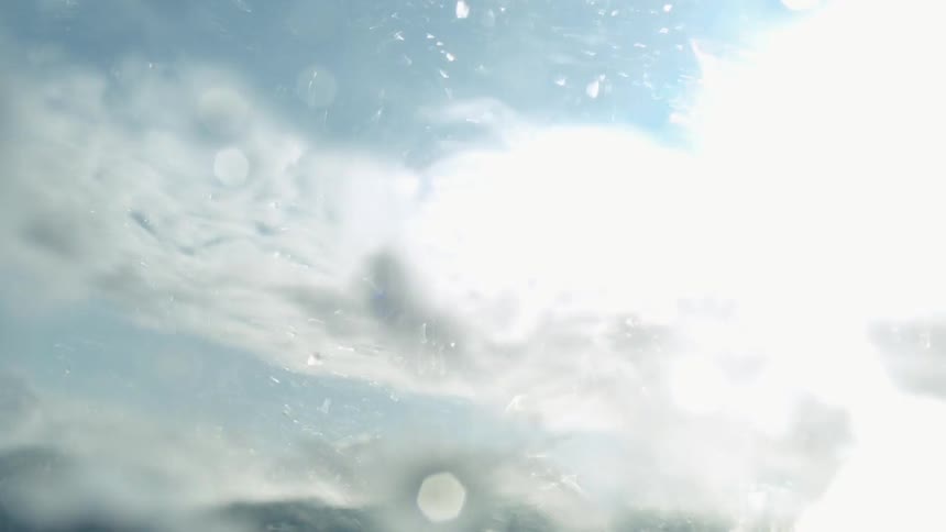 Crystal clear ocean wave crashing against a partly cloudy sky