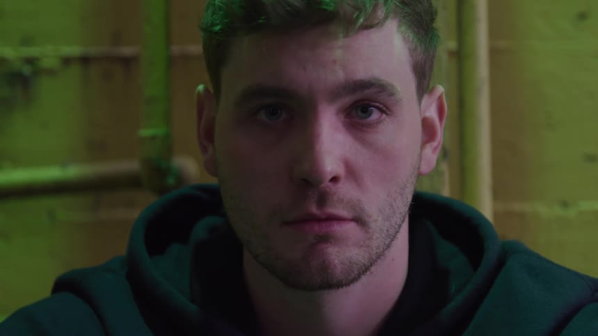 A man wearing a black jacket sits indoors looking sad