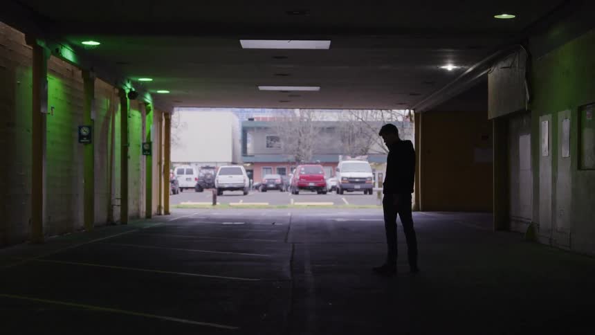 A man paces back and forth talking on the phone inside a garage at midday