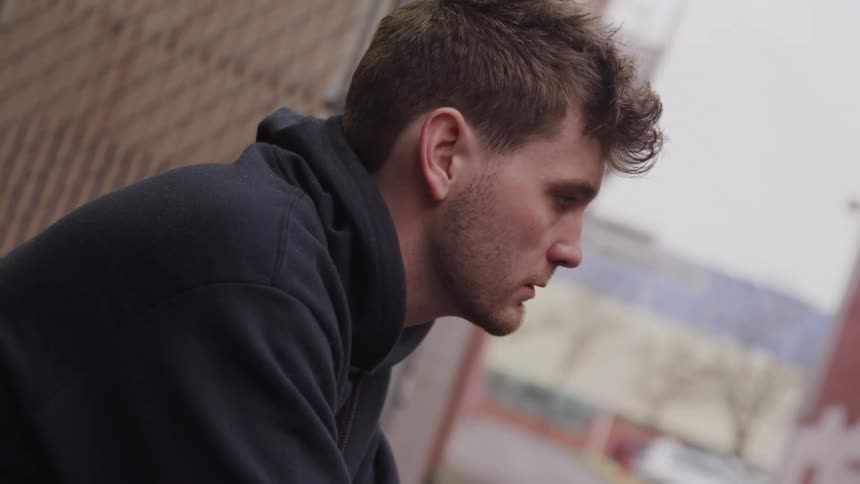 Man sits outside a building near an empty street during the daytime
