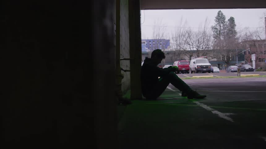 Silhouette of a person sitting leaning against a wall in a parking lot