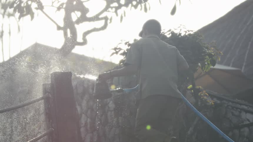 The man is spraying a hose in the yard