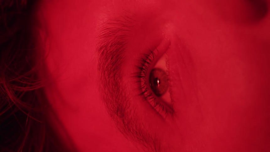 Colored lighting tints a man red as he opens his eye