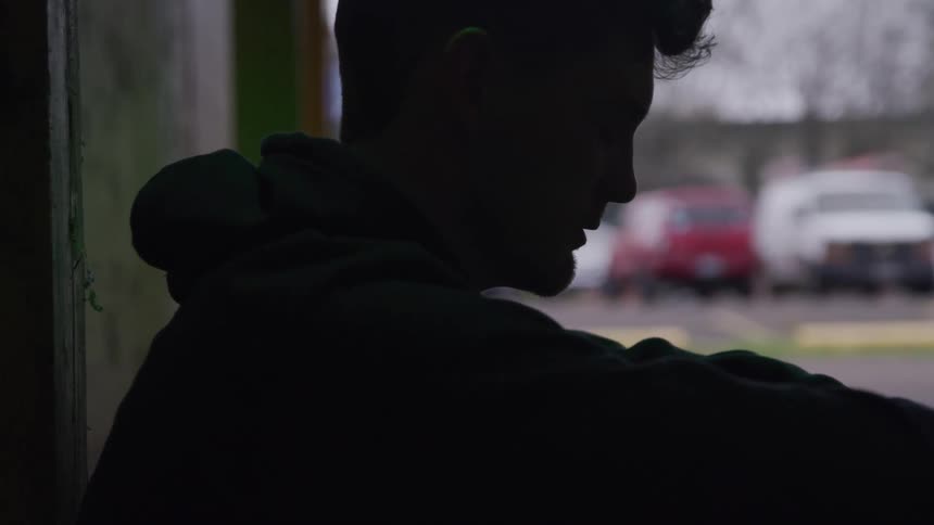 Man sitting on the floor with his back against the wall and head down near a parking garage exit