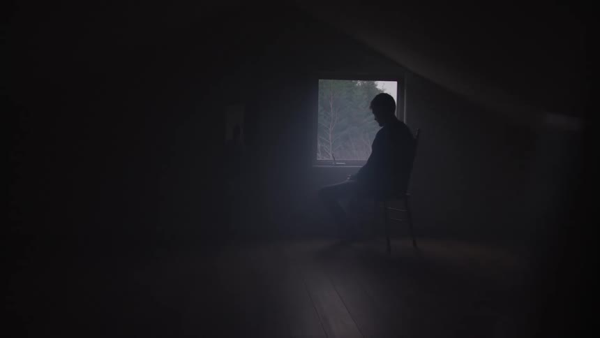 Man sitting on a chair in an empty room facing a window