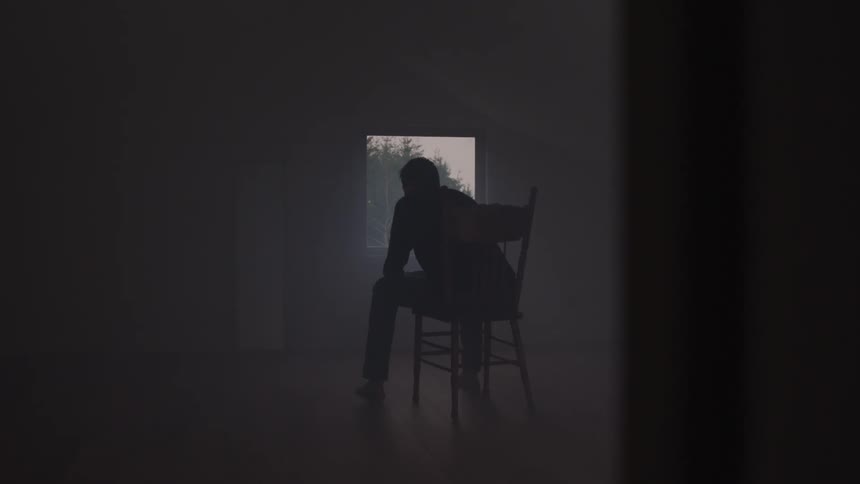 A man sits on a chair inside an empty room deep in thought at sunset