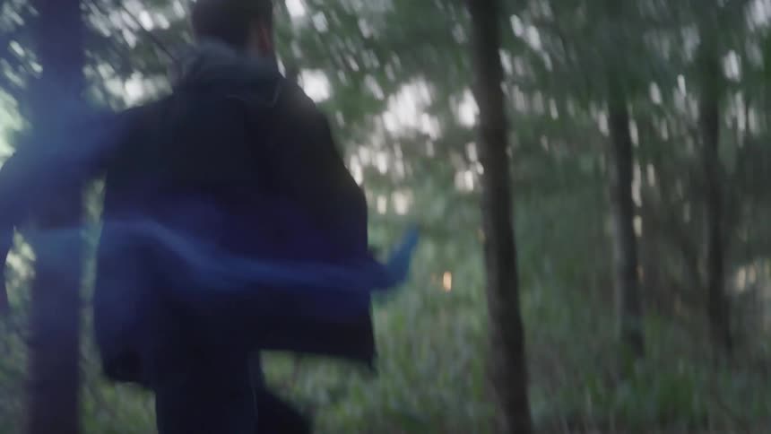 Man running through the forest with an object that releases blue smoke