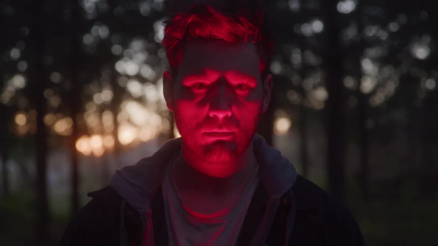Red light on a mans face in a forest at dusk