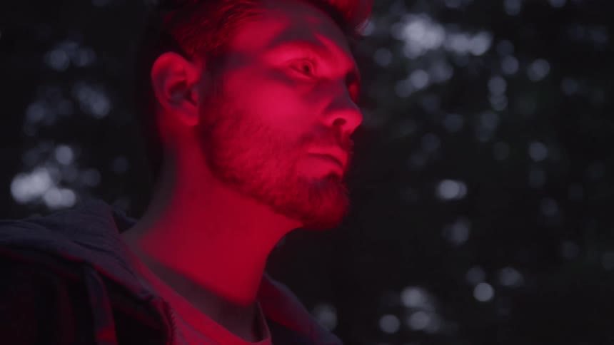 Man in a forest at night with a red light on his face
