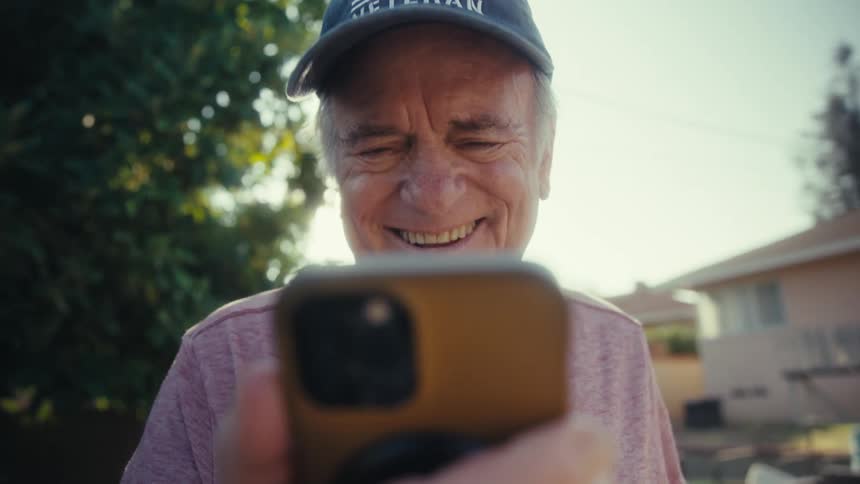 Elderly man with happy expression walking and interacting with smartphone