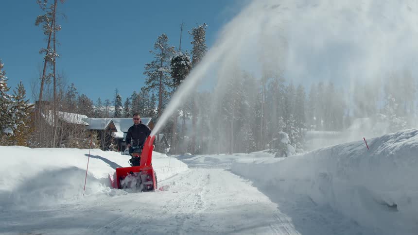 A man using a snow blower to clear a snowcovered road