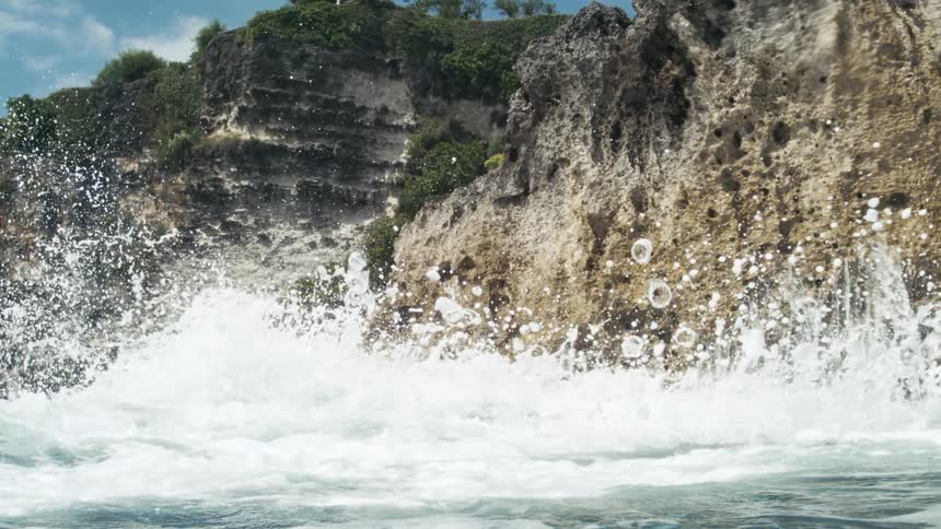 Breaking wave splashes against a rough seaside cliff on a cloudy day