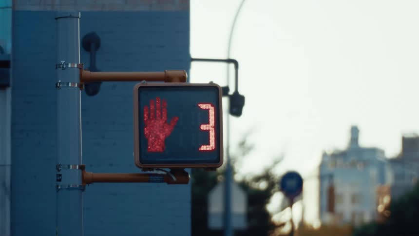 A red hand signal on a pedestrian crosswalk sign glows against the backdrop of a softly lit urban street