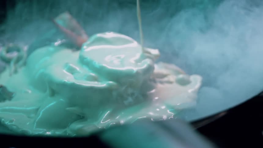 Cream is being poured over vegetables cooking in a pan