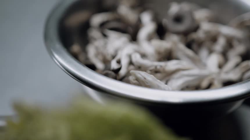 Metal bowl contains raw mushrooms of various shapes and sizes