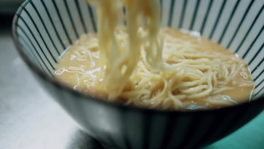 Close up of a person turning noodles in a bowl with a tong