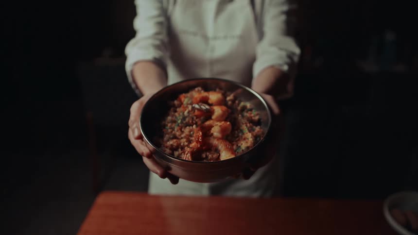 A happy chef in uniform presents a bowl of hearty food with both hands offering it proudly