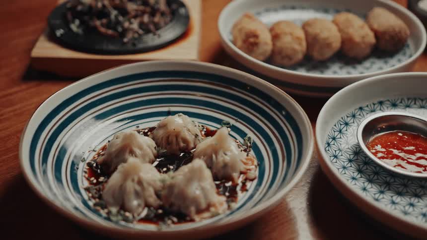 Dumplings and appetizers are served in patterned bowls on a wooden table