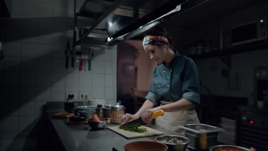 A woman chops vegetables on a cutting board with a knife inside the kitchen