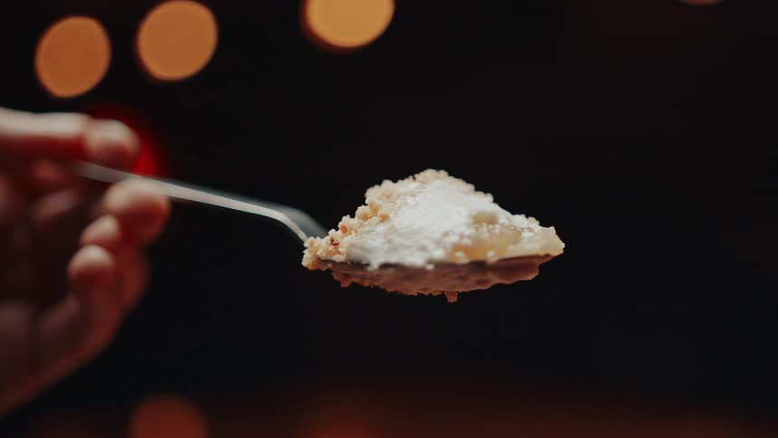 A hand holds a spoon presenting a delightful mouthful of textured dessert set against a softly blurred backdrop of warm festive lights