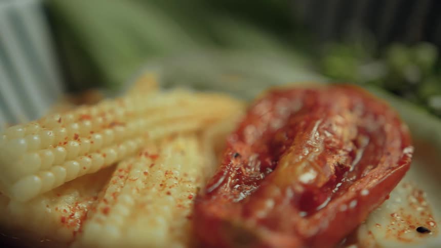 A closeup shot reveals seasoned baby corn and vegetables in a striped bowl