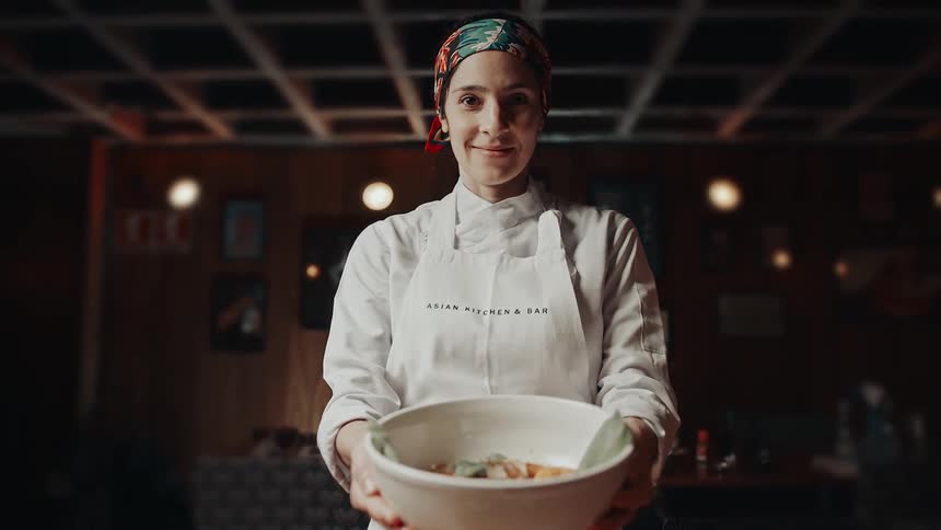 A female chef holds a large bowl of soup while standing in a restaurant